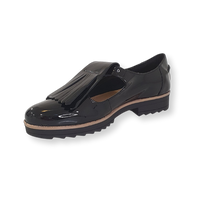 Black patent leather loafer with fringe detail and low heel on black background