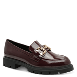 A single burgundy patent leather loafer with a chunky black lug sole and a gold-tone horsebit detail on the strap, shown against a solid green background.