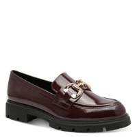 A single burgundy patent leather loafer with a chunky black lug sole and a gold-tone horsebit detail on the strap, shown against a solid green background.