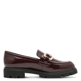 A single burgundy patent leather loafer with a gold-tone horsebit buckle and a chunky black lug sole, shown in profile against a solid green background.