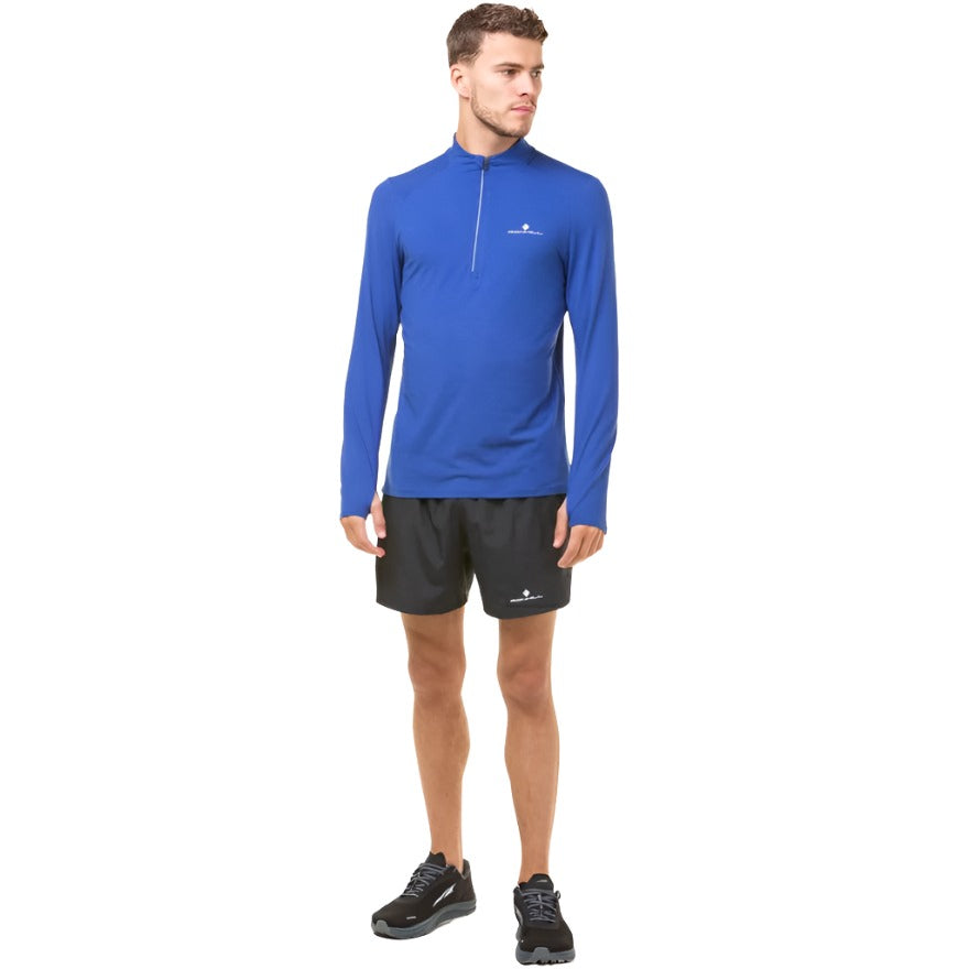 Man wearing a cobalt blue long-sleeve athletic top with zipper, black running shorts and trainers