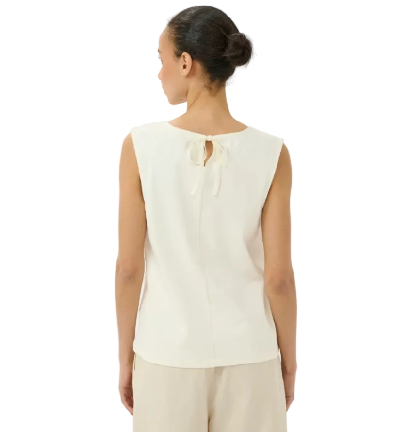 Woman wearing a white sleeveless top with a subtle pattern on a plain background