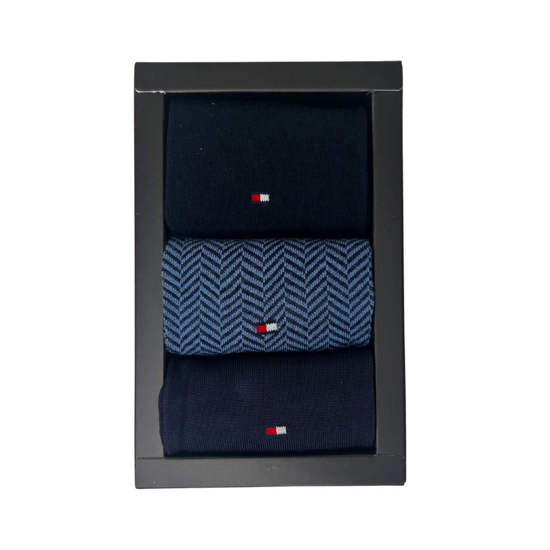 Boxed set of three navy men’s socks, one pair with blue herringbone pattern and small flag logo.