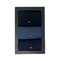 Boxed set of three navy men’s socks, one pair with blue herringbone pattern and small flag logo.
